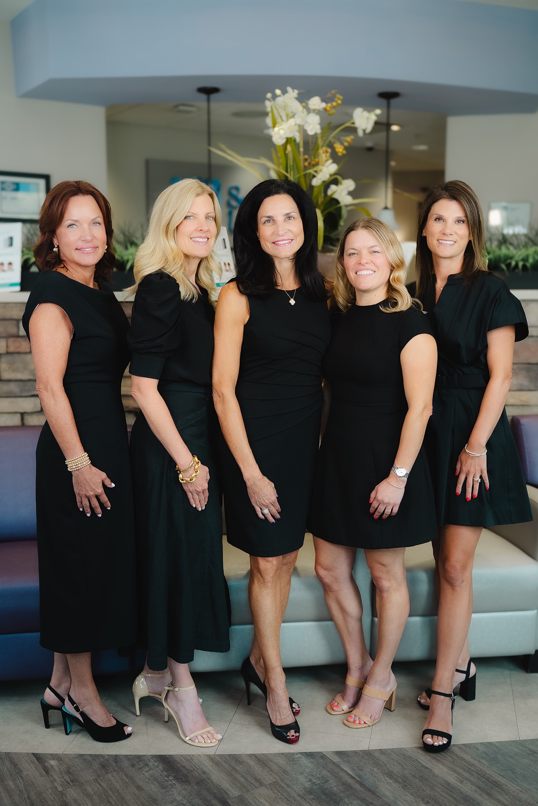 Group of women in black dresses smiling together.